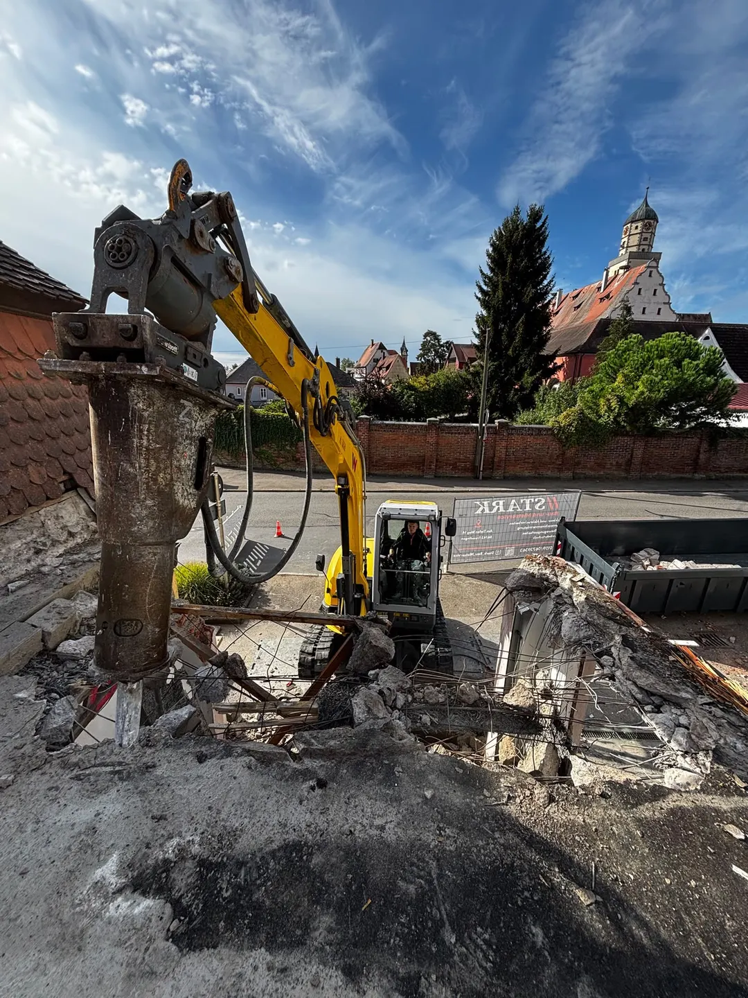 Blick von oben auf den Hydraulikhammer, darunter der gelbe Bagger von Stark beim Abbruch im Ortskern