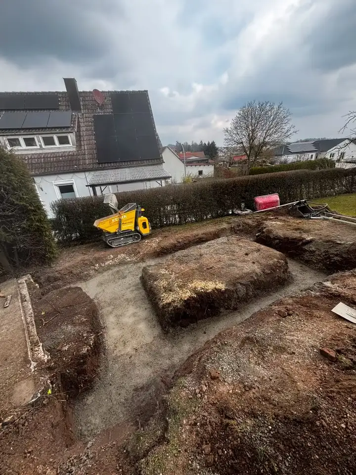 Ausgehobene Grube im Garten, im Hintergrund der Kettendumper