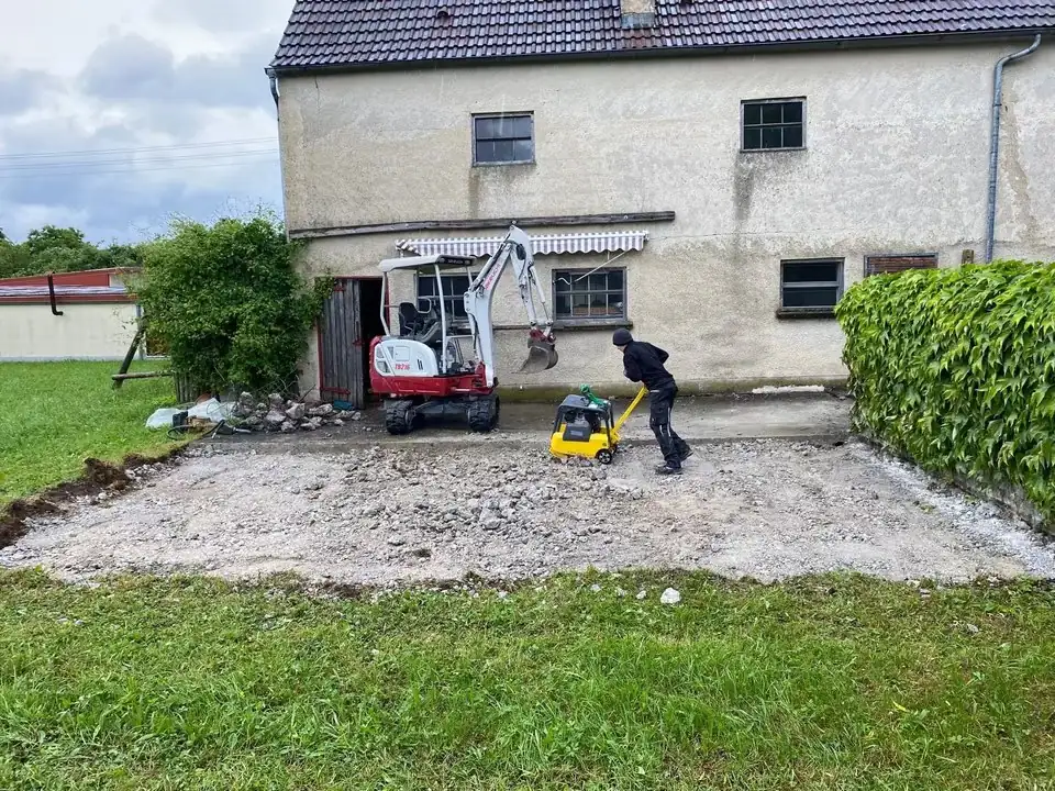 Minibagger und Kettendumper auf einer Schotterfläche vor einem Haus