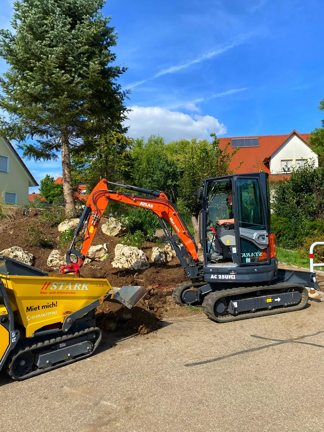 Minibagger Atlas AC 25 UF belädt den gelben Stark-Kettendumper mit Erdaushub am Hang