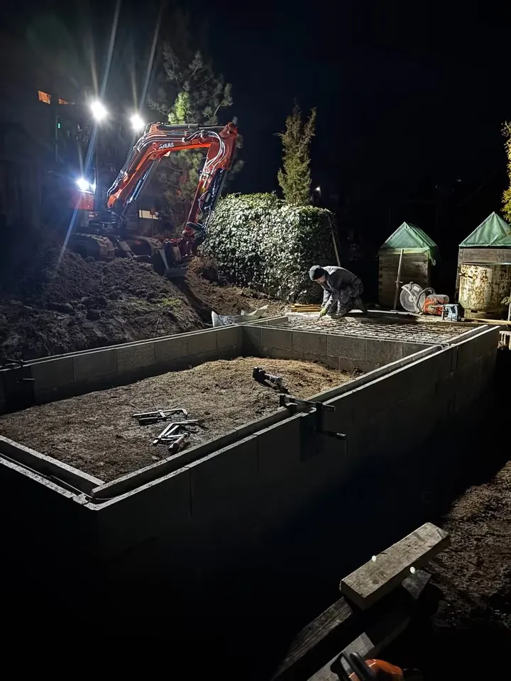 Gesetzte Schalsteine mit Bewehrung bei Nacht, im Hintergrund der Minibagger im Scheinwerferlicht