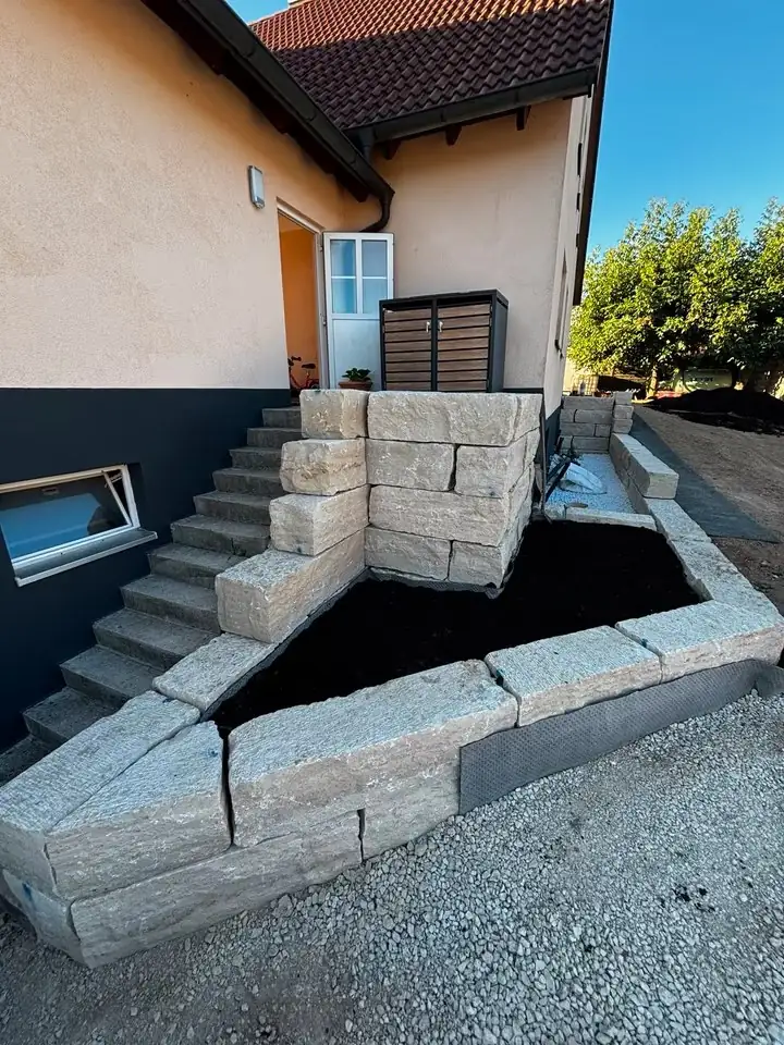 Natursteinmauer mit Betontreppe neben einem Hauseingang
