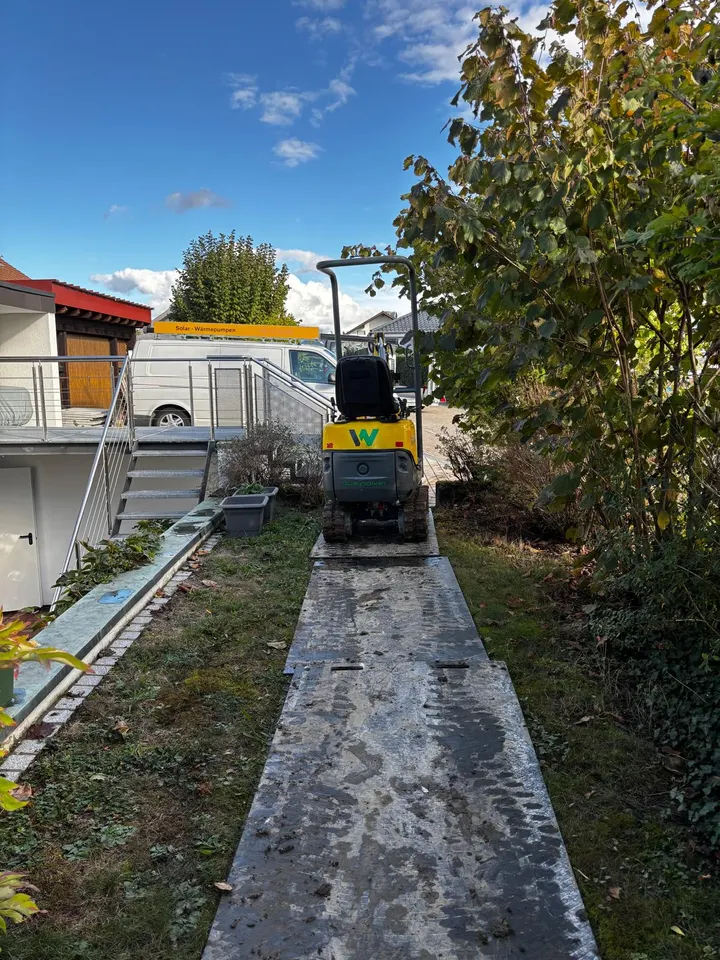 Minibagger fährt auf Baggermatten über den Rasen zum Standort der Wärmepumpe