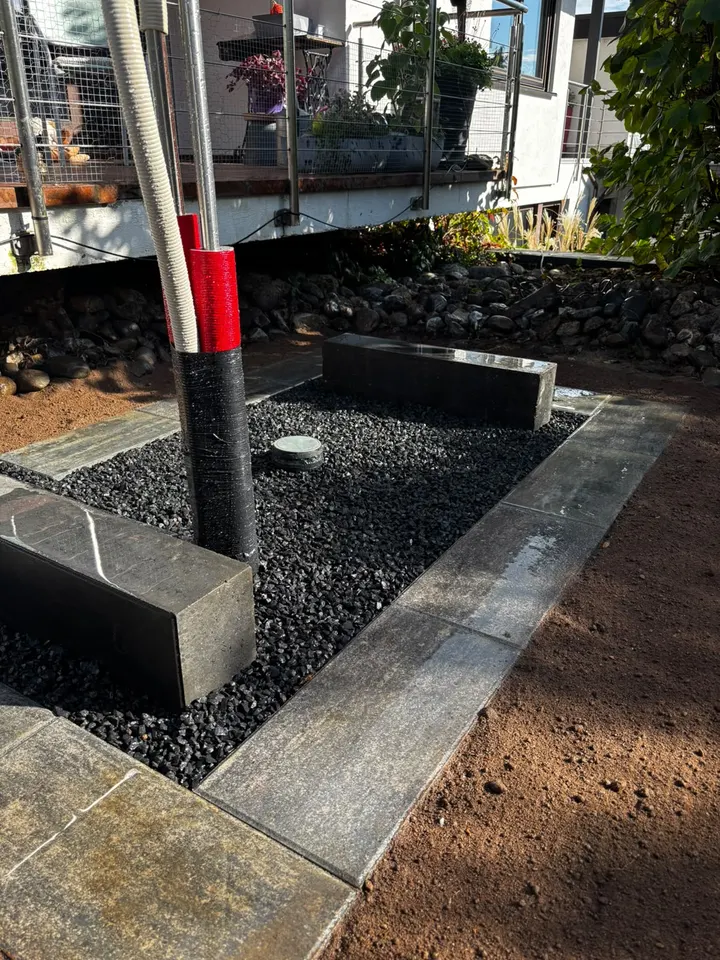 Wärmepumpenfundament mit Randsteinen und dunklem Zierkies in Nahaufnahme