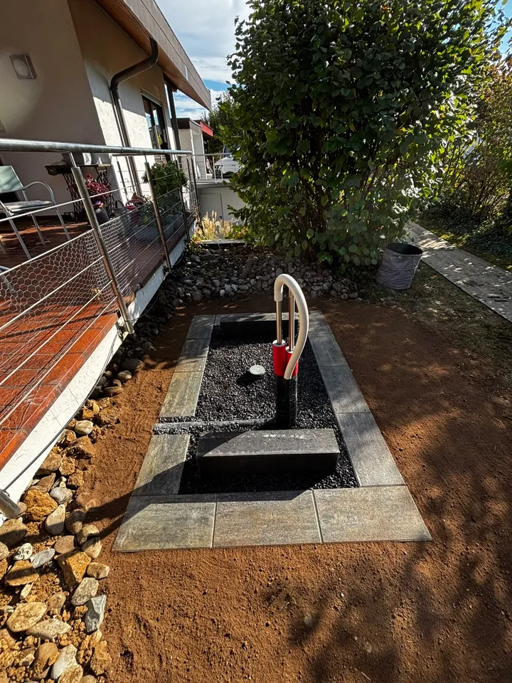 Fertiges Wärmepumpenfundament mit zwei Betonsockeln, Randsteinen und dunklem Zierkies neben einer Hausterrasse